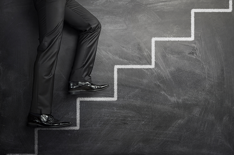 Close up of businessman walking up the career stairs drawn on a black chalkboard with copy space