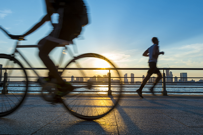 Silhouettes of jogger running and bicyclist cycling at sunset in front of the city skyline ; Shutterstock ID 426768184